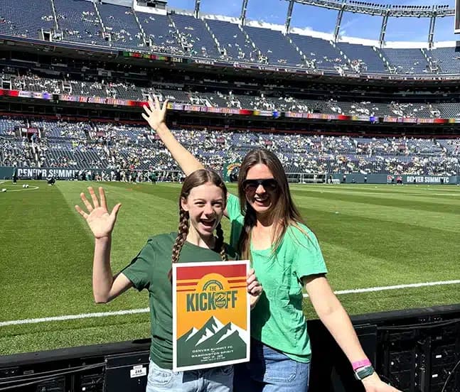 Mighty Pine HVAC owner's family holding a Denver Summit FC Kick Off match poster on the sideline at Empower Field