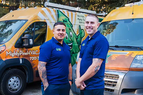 Two smiling service technicians standing in front of the Mighty Pine service truck fleet.