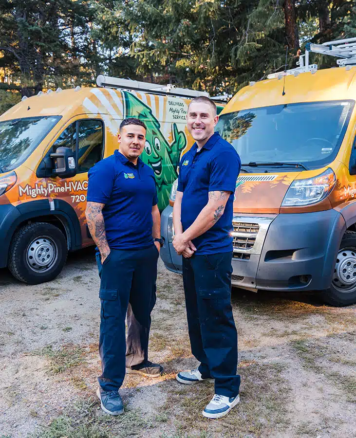 Two smiling service technicians standing in front of the Mighty Pine service truck fleet.