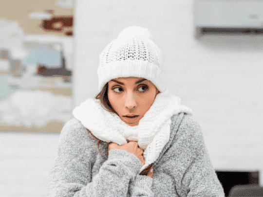 woman wearing hat, scarf and jacket inside home because heater is broken
