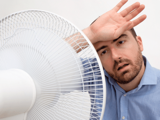man in front of fan, trying to cool down because AC is broken